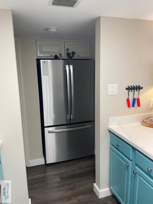 kitchen with dark wood-style floors, blue cabinetry, light countertops, visible vents, and freestanding refrigerator