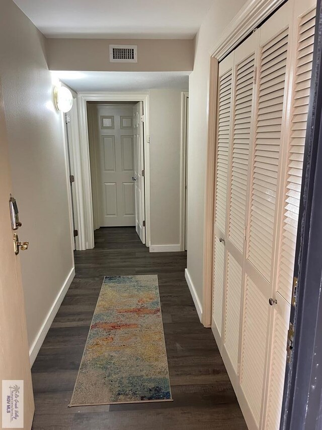 hallway featuring dark wood-style flooring, visible vents, and baseboards