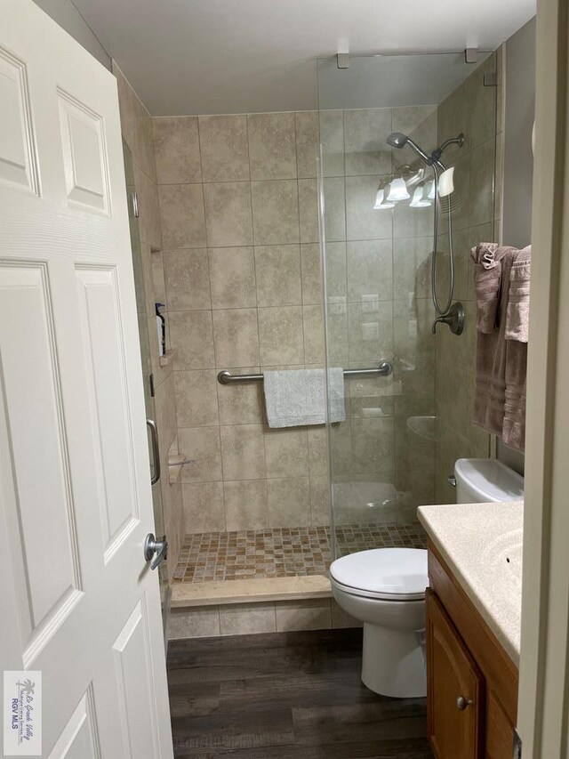 bathroom featuring wood finished floors, a stall shower, vanity, and toilet