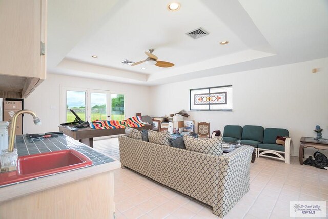 living room with a raised ceiling, ceiling fan, sink, and light tile patterned floors