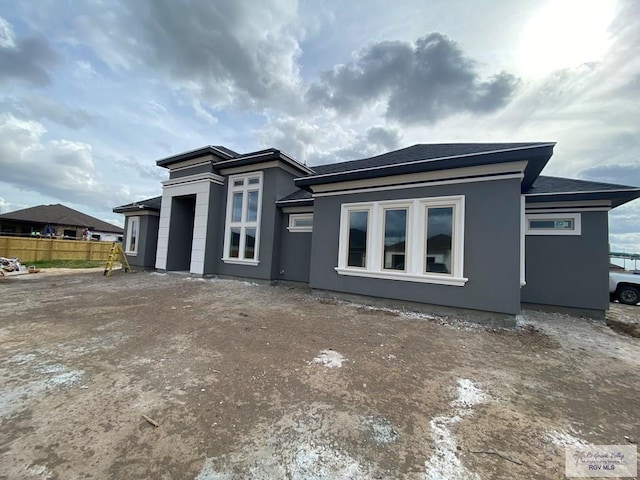 view of front facade featuring roof with shingles, fence, and stucco siding