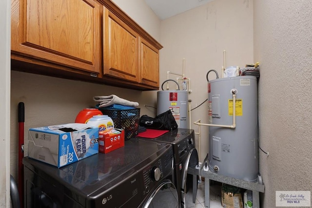 clothes washing area with cabinets, electric water heater, washing machine and dryer, and tile patterned flooring