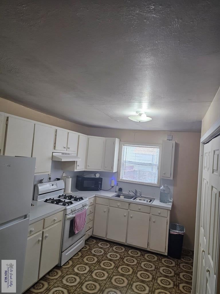 kitchen featuring a textured ceiling, sink, white cabinets, and white appliances