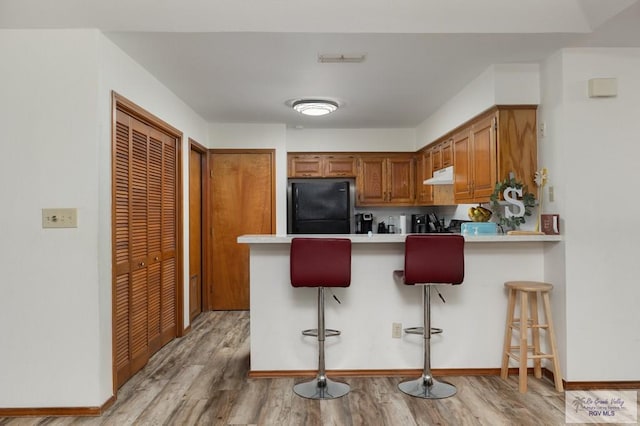 6246 Camelot Dr, Harlingen, TX 78550 - kitchen with freestanding refrigerator, brown cabinets, light countertops, under cabinet range hood, and a peninsula