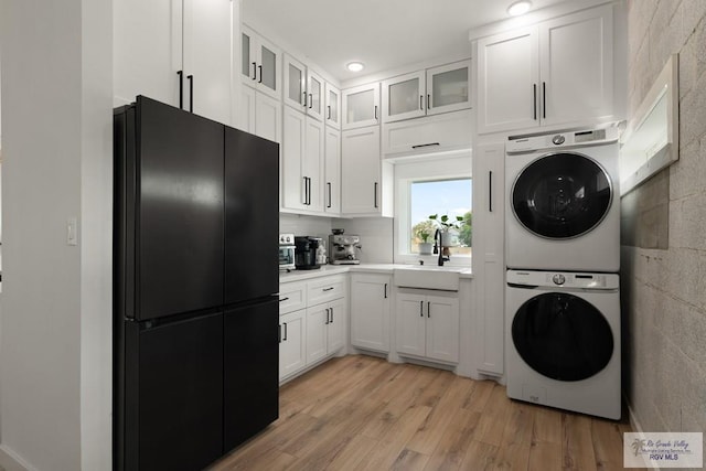 washroom with sink, stacked washing maching and dryer, and light hardwood / wood-style flooring