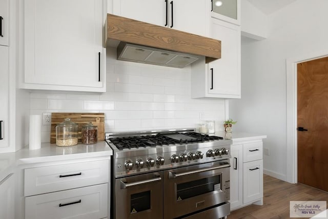 kitchen with decorative backsplash, white cabinets, wood-type flooring, and range with two ovens