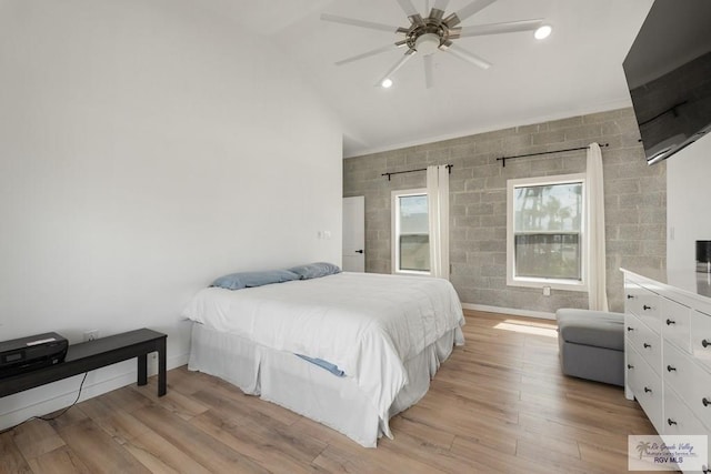 bedroom featuring ceiling fan, tile walls, light hardwood / wood-style flooring, and vaulted ceiling