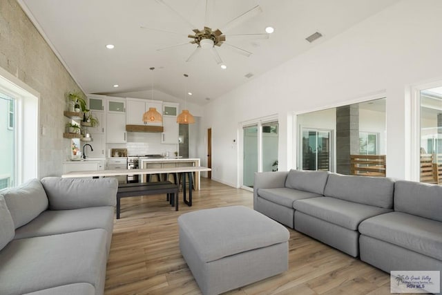 living room featuring high vaulted ceiling, light hardwood / wood-style flooring, ceiling fan, and sink