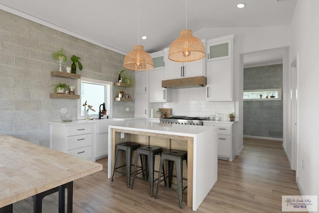 kitchen with a kitchen breakfast bar, sink, light hardwood / wood-style flooring, vaulted ceiling, and white cabinetry