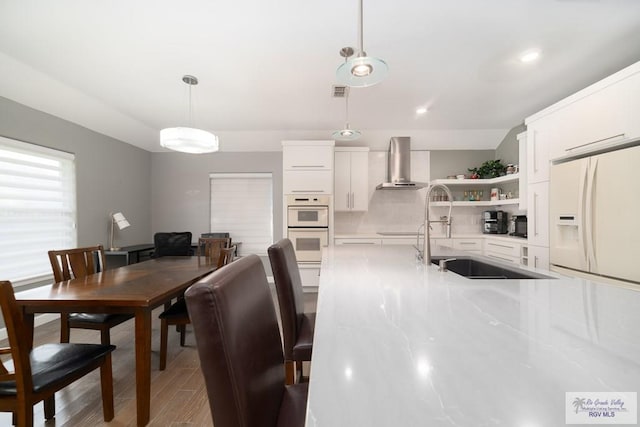 kitchen with white appliances, a sink, white cabinetry, wall chimney range hood, and open shelves