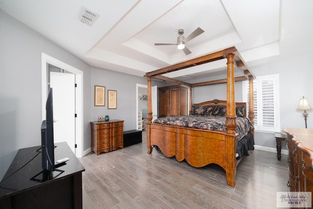 bedroom featuring a tray ceiling, visible vents, light wood-style floors, a ceiling fan, and baseboards