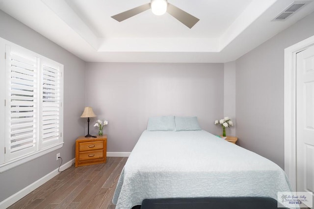 bedroom featuring wood finished floors, a ceiling fan, visible vents, baseboards, and a raised ceiling