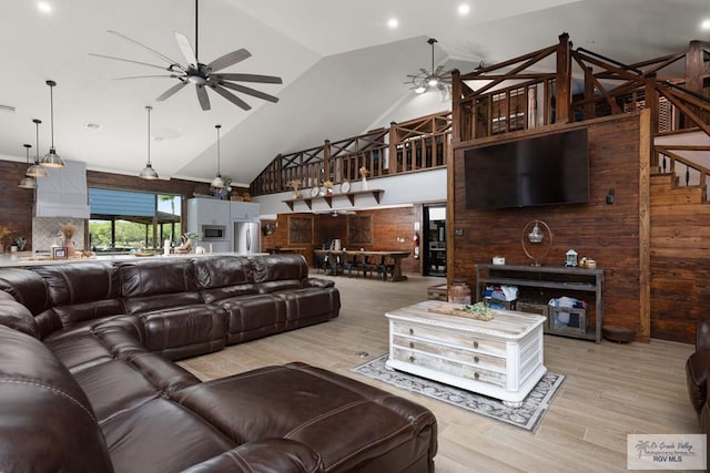 living room with wooden walls, high vaulted ceiling, and light hardwood / wood-style floors