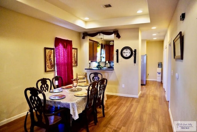 dining area with a raised ceiling and light hardwood / wood-style floors