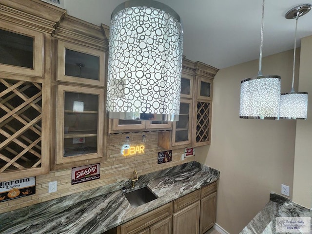 kitchen featuring brown cabinets, pendant lighting, a sink, backsplash, and stone counters