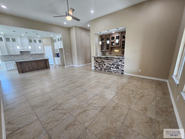 unfurnished living room featuring marble finish floor, a ceiling fan, a sink, recessed lighting, and baseboards