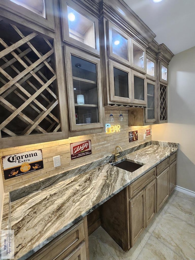 kitchen with marble finish floor, a sink, backsplash, glass insert cabinets, and light stone countertops