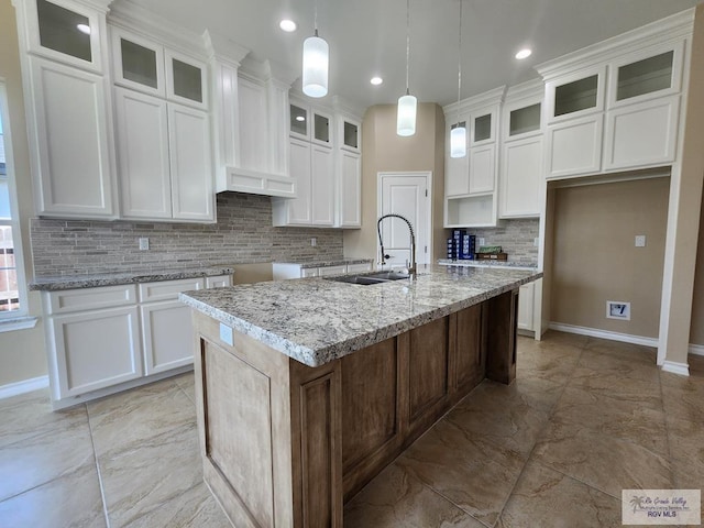 kitchen featuring a sink, marble finish floor, a center island with sink, and white cabinetry