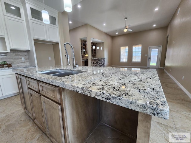 kitchen featuring a sink, ceiling fan, a center island with sink, and white cabinetry