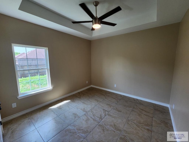 empty room with baseboards, a tray ceiling, and a ceiling fan