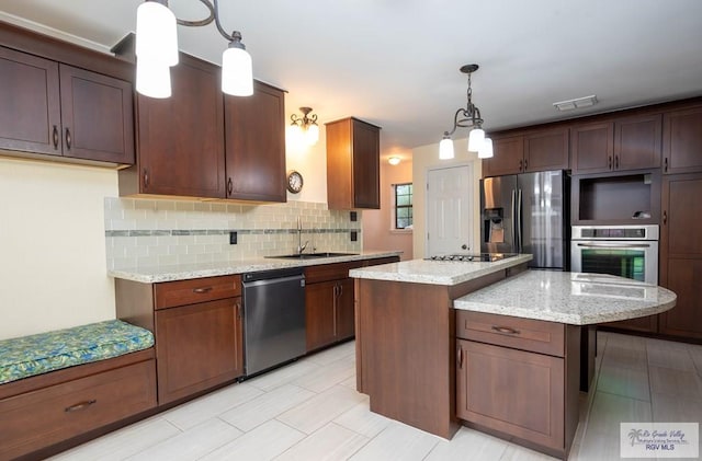 kitchen with sink, hanging light fixtures, appliances with stainless steel finishes, a kitchen island, and light stone counters