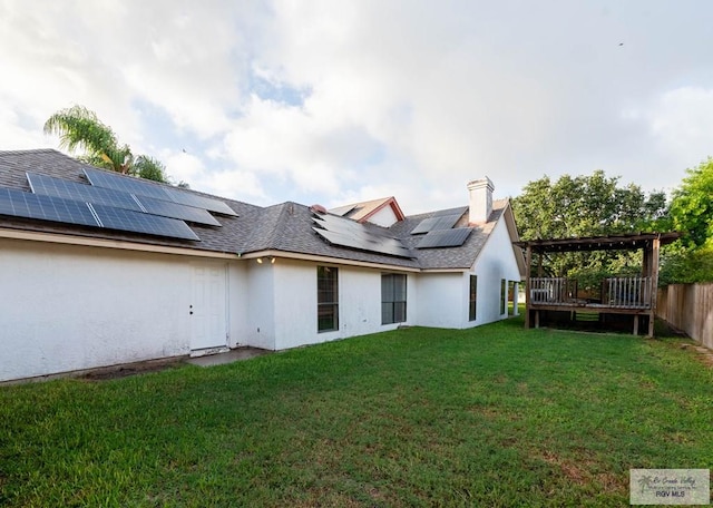 back of property featuring a lawn, solar panels, a deck, and a pergola