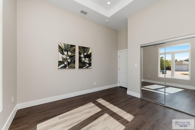 unfurnished bedroom with a closet, dark hardwood / wood-style flooring, and a towering ceiling