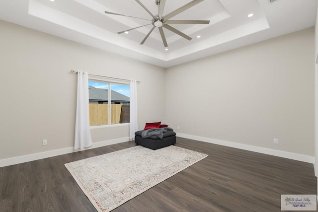 unfurnished room featuring a raised ceiling, ceiling fan, and dark hardwood / wood-style floors