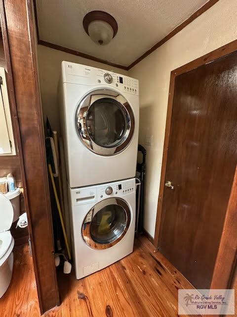 washroom with a textured ceiling, crown molding, light hardwood / wood-style flooring, and stacked washer and clothes dryer