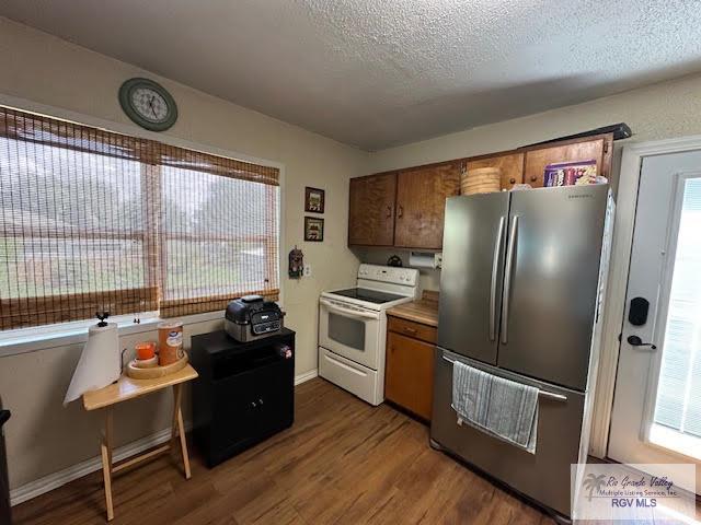 kitchen with white range with electric stovetop, a wealth of natural light, dark hardwood / wood-style flooring, and stainless steel refrigerator