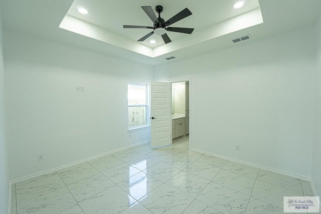 unfurnished bedroom with a tray ceiling, ensuite bath, and ceiling fan