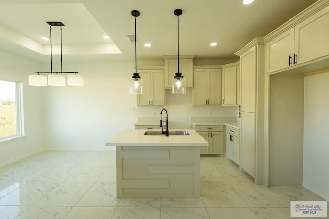 kitchen featuring a kitchen island with sink, sink, hanging light fixtures, and a raised ceiling