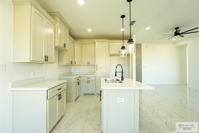 kitchen with ceiling fan, decorative light fixtures, sink, and a center island with sink