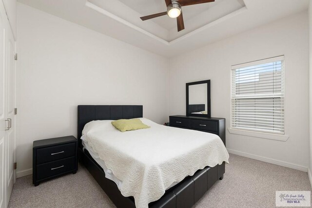 bedroom featuring light colored carpet, a raised ceiling, and ceiling fan