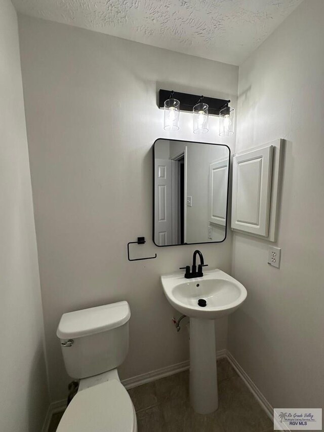 bathroom featuring toilet, a textured ceiling, tile patterned floors, and baseboards