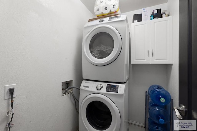 clothes washing area with cabinets and stacked washing maching and dryer