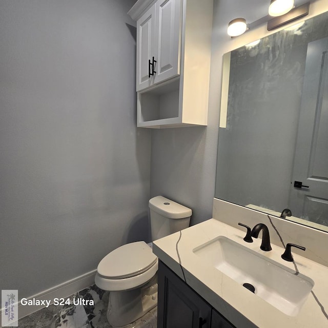 bathroom with baseboards, toilet, vanity, and marble finish floor