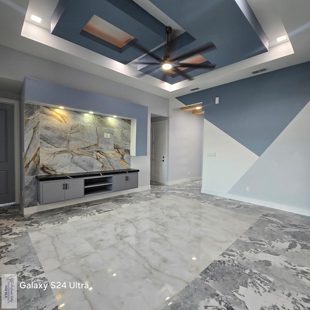 unfurnished living room with marble finish floor, a ceiling fan, visible vents, and a raised ceiling