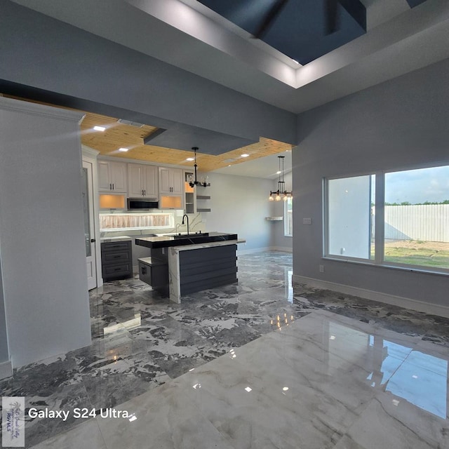 kitchen with stainless steel microwave, an inviting chandelier, marble finish floor, baseboards, and open floor plan