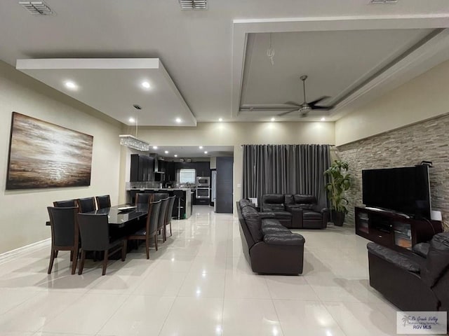 living area with visible vents, a tray ceiling, light tile patterned flooring, and a ceiling fan