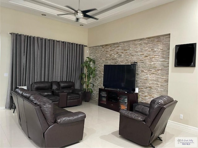 living room featuring a tray ceiling, baseboards, a ceiling fan, and light tile patterned flooring