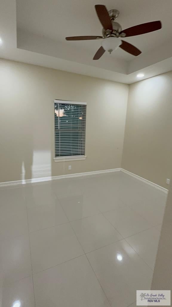 empty room with a raised ceiling, baseboards, and tile patterned floors