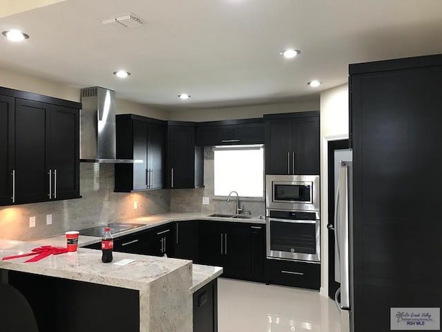 kitchen featuring stainless steel appliances, visible vents, a sink, dark cabinetry, and wall chimney exhaust hood