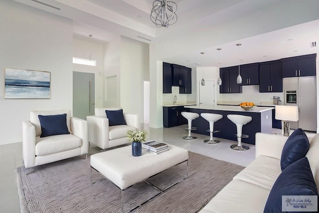 living room featuring sink, a towering ceiling, light tile patterned floors, and a notable chandelier