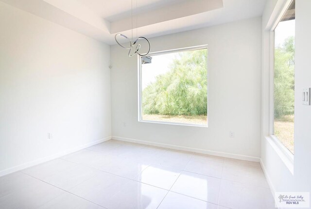 unfurnished dining area featuring light tile patterned floors and a tray ceiling