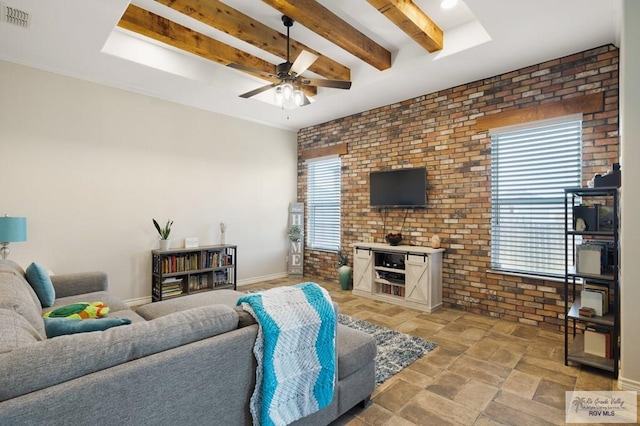 living room with beamed ceiling, ceiling fan, and brick wall