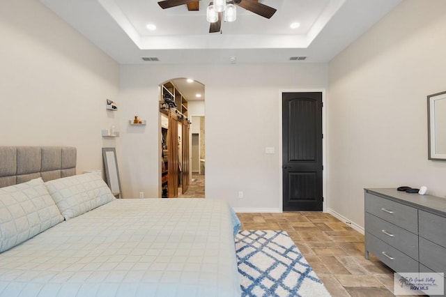 bedroom with a raised ceiling, a walk in closet, and ceiling fan