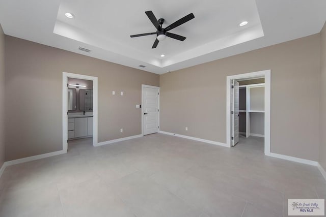 unfurnished bedroom featuring ensuite bath, a walk in closet, a raised ceiling, and ceiling fan