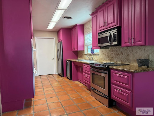 kitchen featuring sink, stainless steel appliances, light tile patterned flooring, decorative backsplash, and dark stone counters