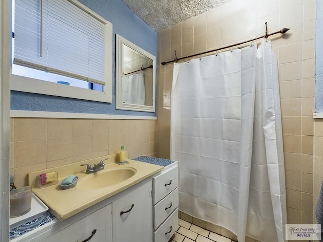 bathroom with tile patterned flooring, vanity, a textured ceiling, and tile walls